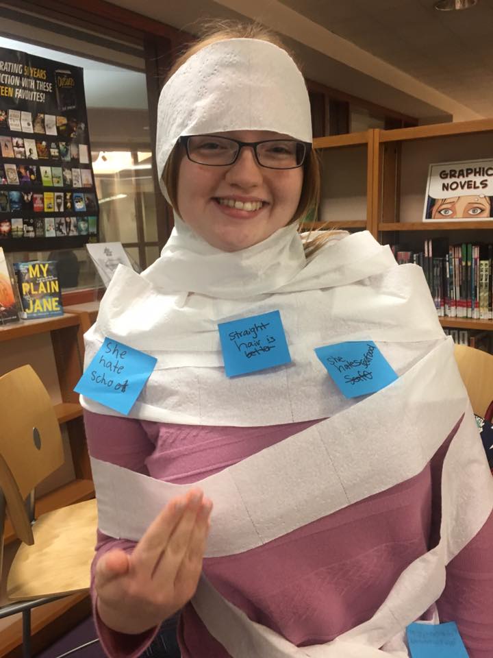 Girl in the library wrapped in toilet paper covered in post-it notes