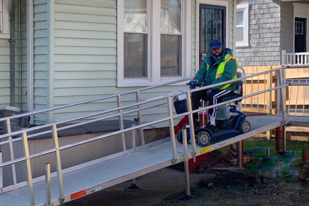 electric wheelchair using a metal ramp set up from the front door of a house
