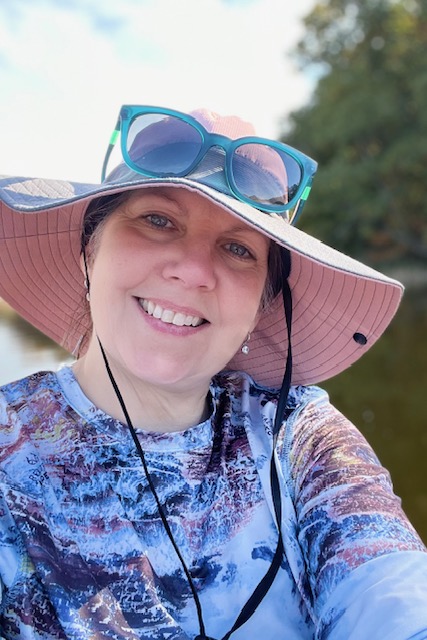 Female Stephanie Schwartz is taking a selfie smiling at the camera. She is wearing a floppy hat and sunglasses on her head. 